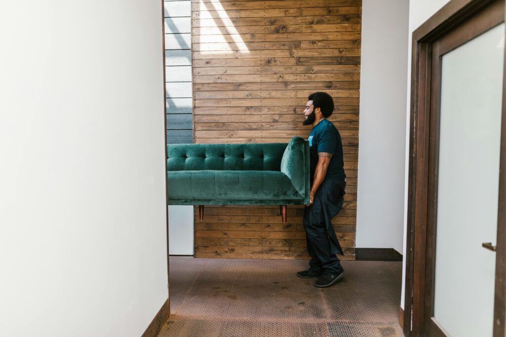 A mover carries a green sofa indoors, showcasing modern interior design and relocation services.